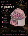 A pink embellished women's cap displayed on a black stand against a dark decorative background. The hat features a large pink floral applique with gold embroidery, butterfly motifs, and rhinestone trim.
